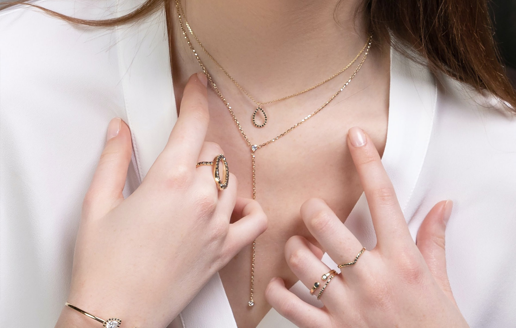 Woman's Neck & Hands. She's Wearing a White Blouse and Gold Necklaces and Rings
